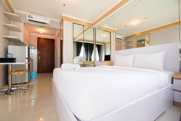A hotel room with a large bed, a desk with a chair, a mirror, and a wardrobe.