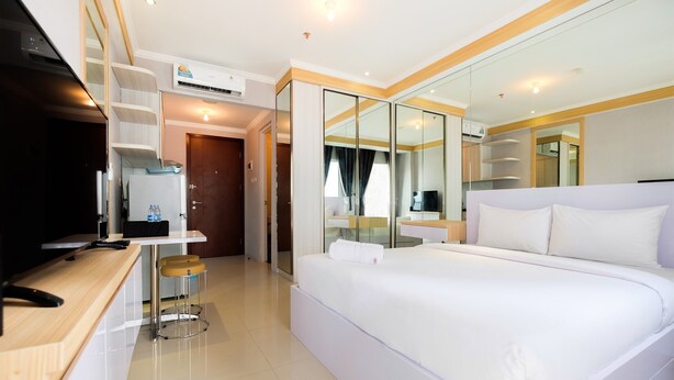 Una habitación de hotel moderna con una cama grande, un escritorio con una silla, un televisor y un espejo.