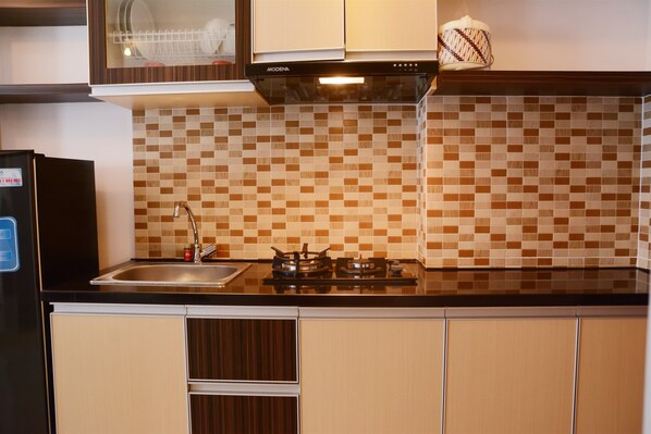 A kitchen with a tiled backsplash, a stove, a sink, and wooden cabinets. - Modern Studio Signature Park Grande Apartment Near Cawang (Jakarta)