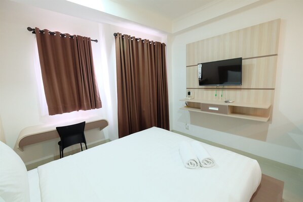 Ein Hotelzimmer mit Bett, Schreibtisch, Stuhl, Fernseher und Ablagefläche mit Fernbedienung.