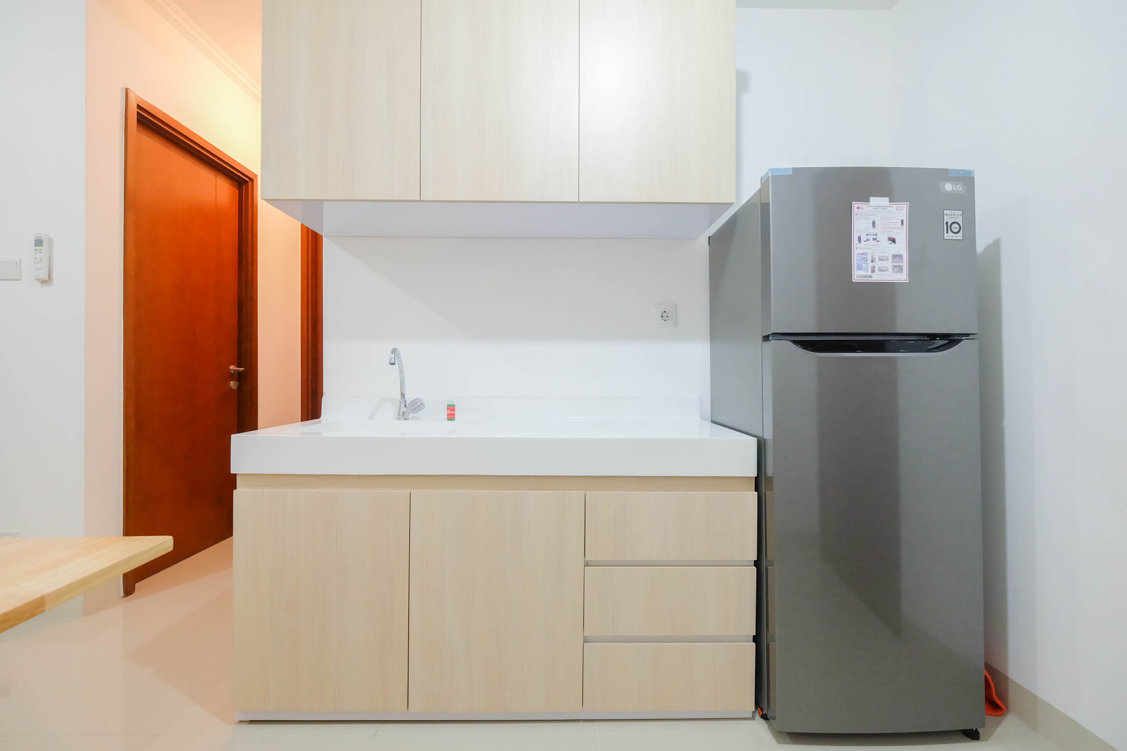 A kitchen with a stainless steel refrigerator, wooden cabinets, a white countertop, and a wooden door.