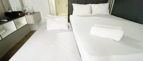 A hotel room with a bed, white linens, a bedside table with a lamp, and a door leading to another room.