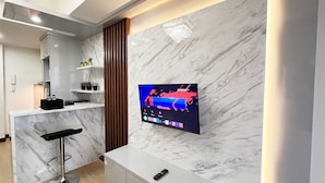 Une cuisine moderne avec un dosseret en marbre, un bar intégré et un téléviseur fixé au mur diffusant une chaîne de sport.