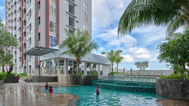 Un espace piscine doté d’une terrasse en bois, entouré de palmiers et bordé d’un bâtiment moderne avec des balcons.