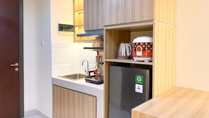 A compact kitchen with a built-in stove, a coffee maker, and a refrigerator. - Nice And Cozy Studio At Pollux Chadstone Apartment (Cikarang)