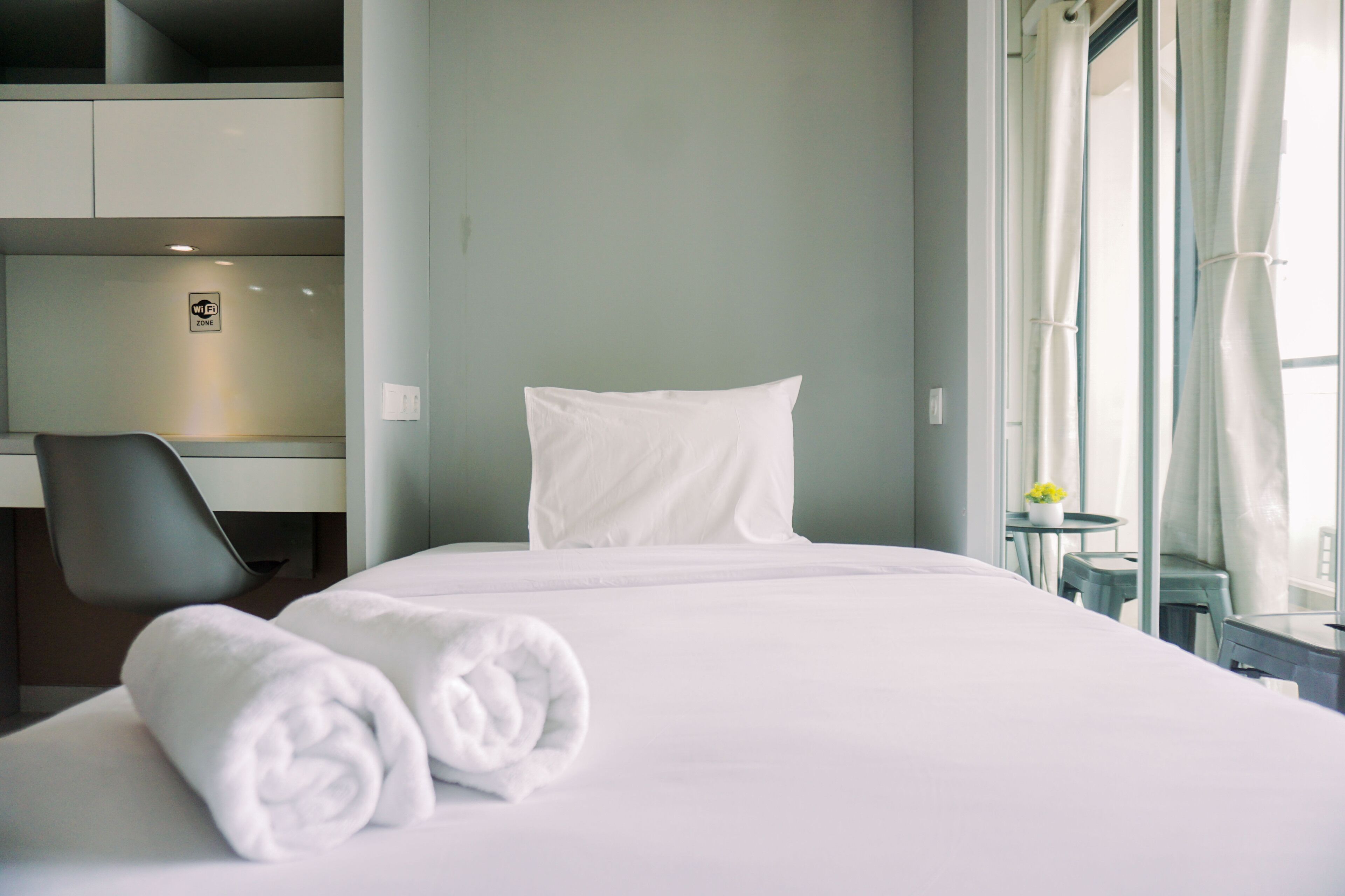 Habitación de hotel con una cama bien hecha, una silla, una mesita con una planta y una ventana con cortinas.