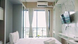A hotel room with a bed, a TV mounted on the wall, and a window with curtains. - Best Deal And Strategic Studio Sky House Bsd Apartment (Pagedangan)