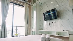 A hotel room with a large bed, a mounted TV, and a view of the city. - Best Deal And Strategic Studio Sky House Bsd Apartment (Pagedangan)