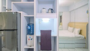 A compact room with a refrigerator, a water dispenser, a bed, and a small table with a chair. - Good And Homey Studio At Kebagusan City Apartment (Jakarta)