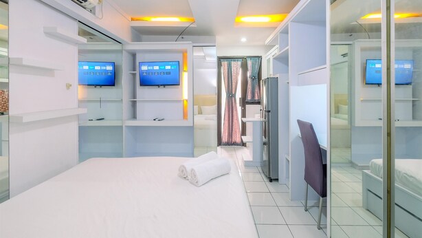 A modern hotel room with a bed, a desk, a chair, a TV, and a wardrobe. - Good And Homey Studio At Kebagusan City Apartment (Jakarta)