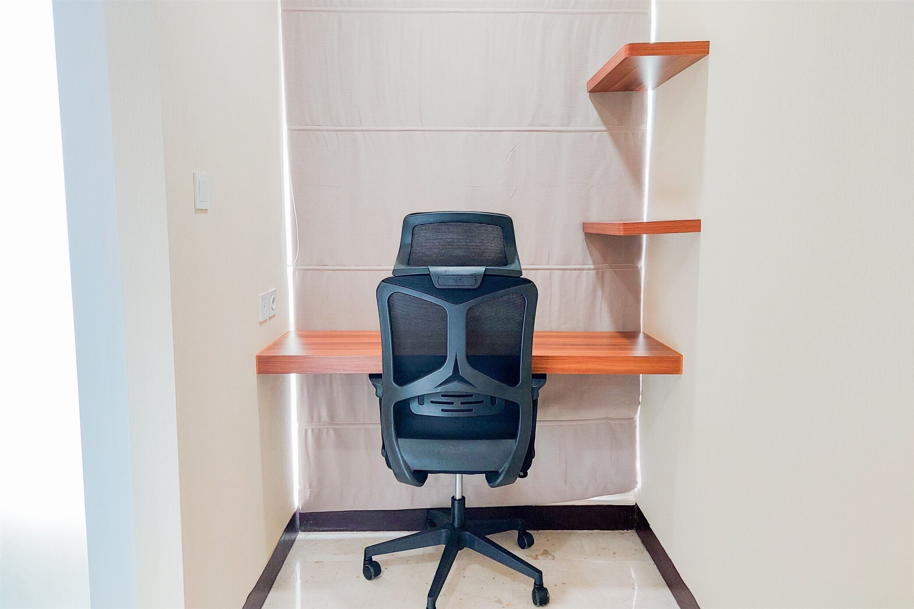 A modern office chair with a mesh backrest and a five-point base, positioned in front of a white wall with a wooden shelf unit.