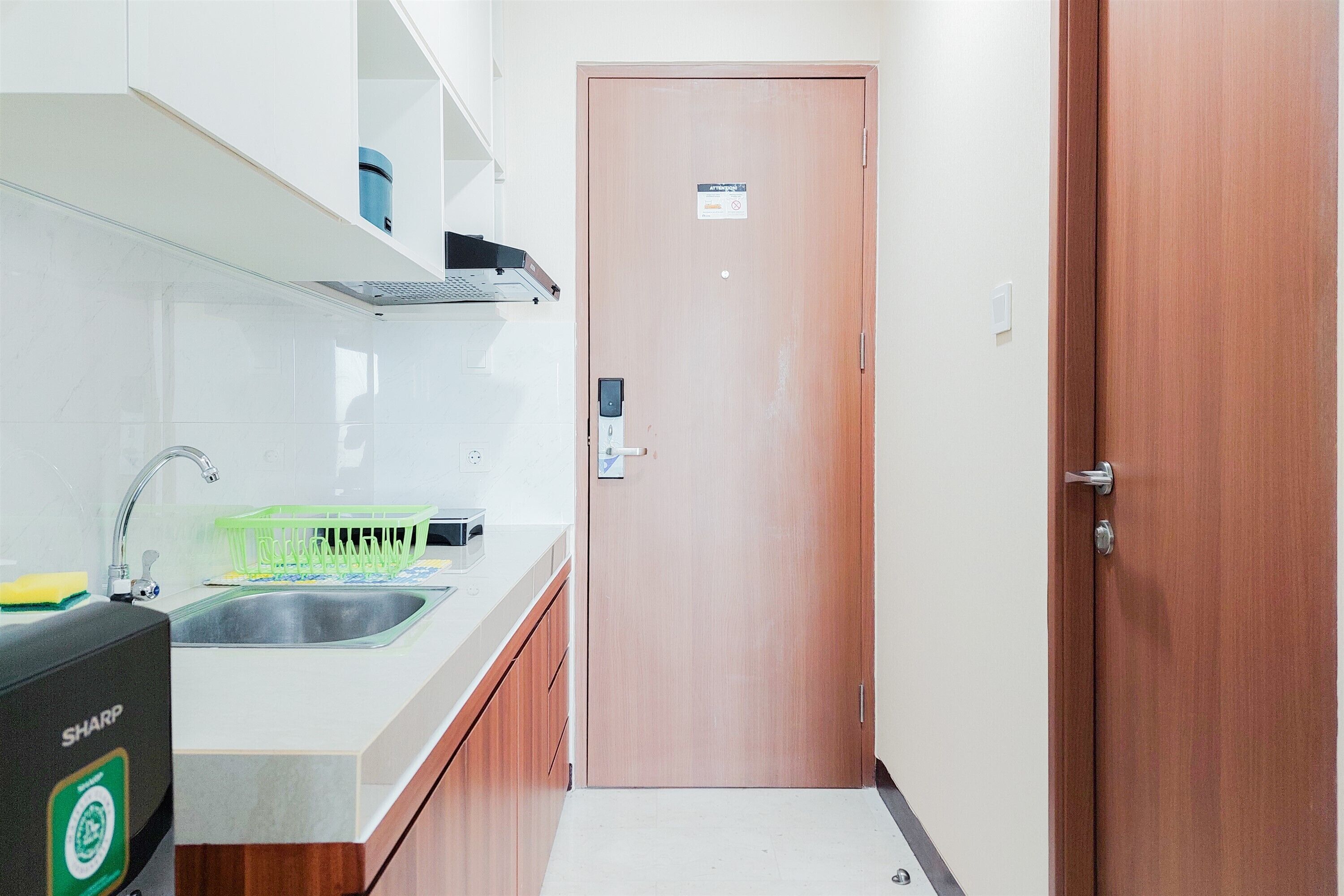 A small kitchen with a sink, a microwave, and a dish rack. There is a wooden door with a sign above it.