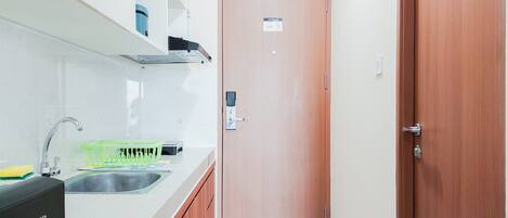 A small kitchen with a sink, a microwave, and a dish rack. There is a wooden door with a sign above it.