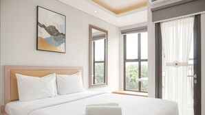 A hotel room with a large bed, a headboard, a painting on the wall, and a window with curtains. - Warm And Minimalist Studio Transpark Bintaro Apartment (South Tangerang)