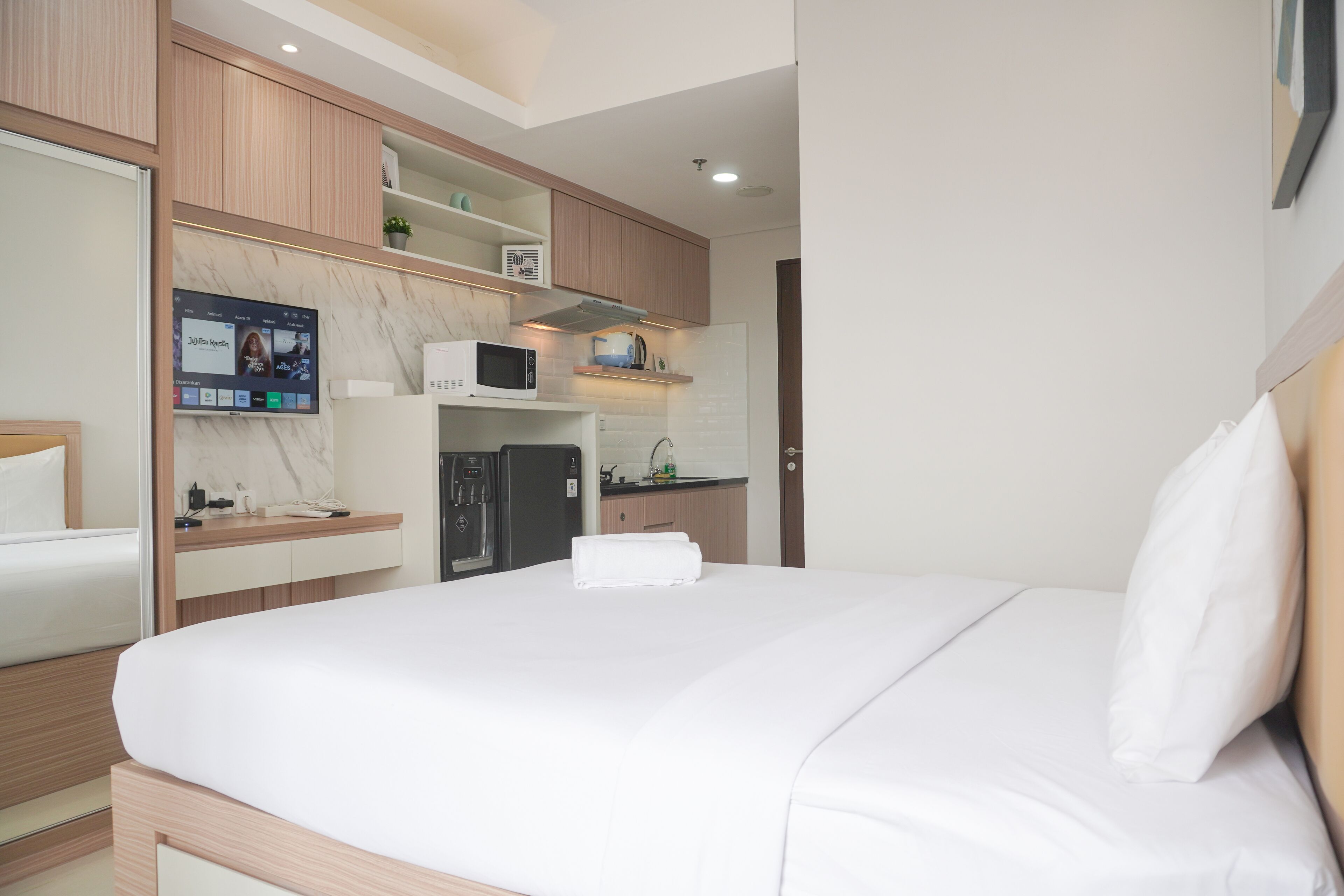 A hotel room with a bed, a TV mounted on the wall, a microwave, and a refrigerator.