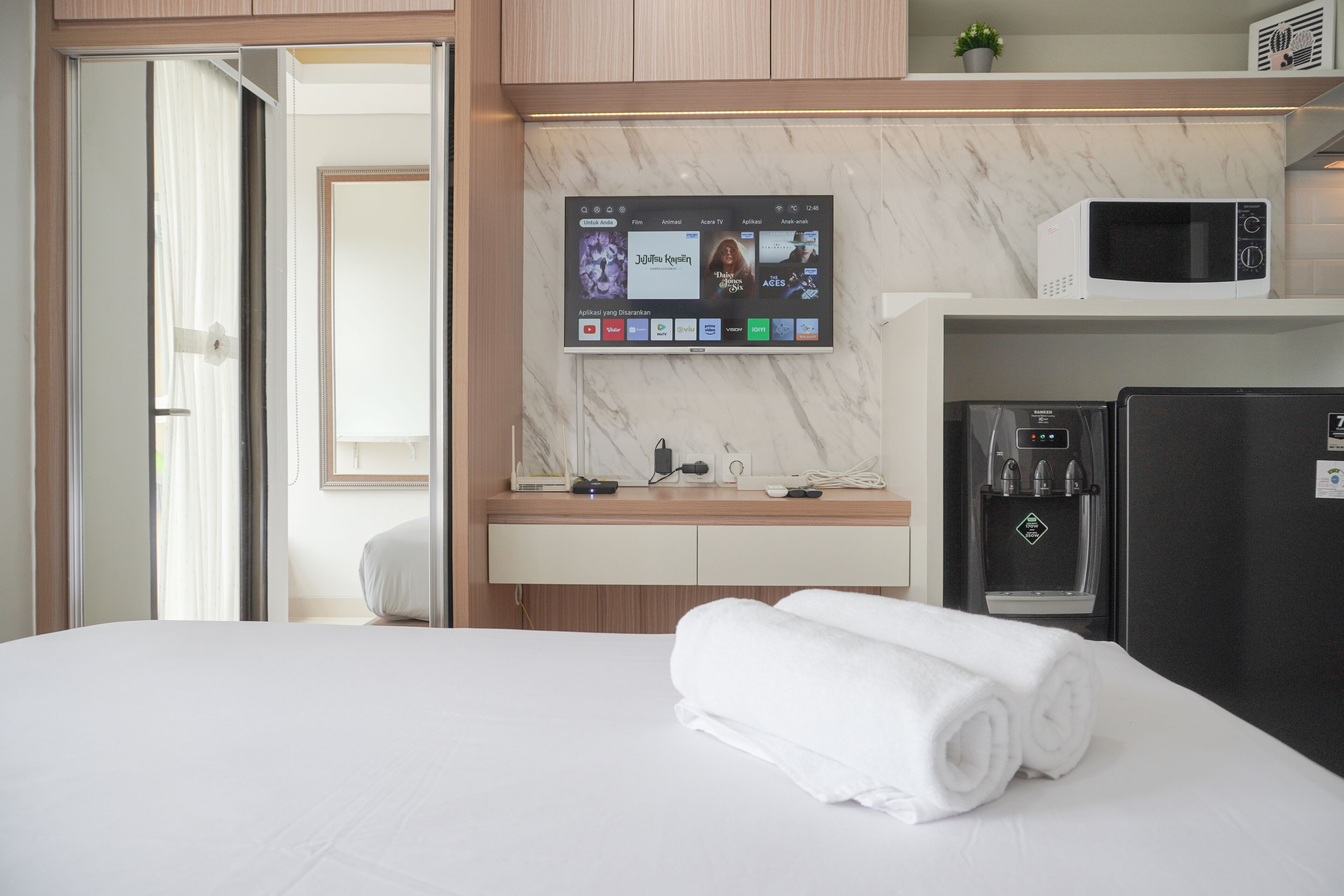 A hotel room with a bed, a TV mounted on the wall, a microwave, and a refrigerator.