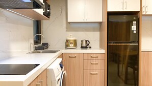A modern kitchen with a built-in oven, a stainless steel refrigerator, wooden cabinets, and a countertop with a kettle and coffee maker. - Cozy Living And Comfort 3Br Meikarta Apartment (Cikarang)