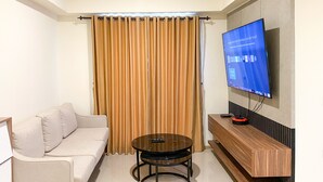 A living room with a sofa, a coffee table, a flat-screen TV mounted on the wall, and a curtain. - Cozy Living And Comfort 3Br Meikarta Apartment (Cikarang)