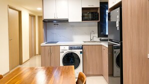 A compact kitchen with a built-in washing machine, a microwave, and a refrigerator. - Cozy Living And Comfort 3Br Meikarta Apartment (Cikarang)
