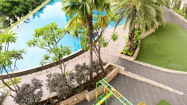A swimming pool surrounded by greenery, a children's play area, and a well-maintained lawn.