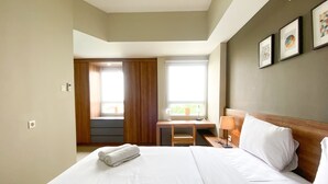 A hotel room with a large bed, a desk with a lamp, a window with curtains, and framed pictures on the wall.