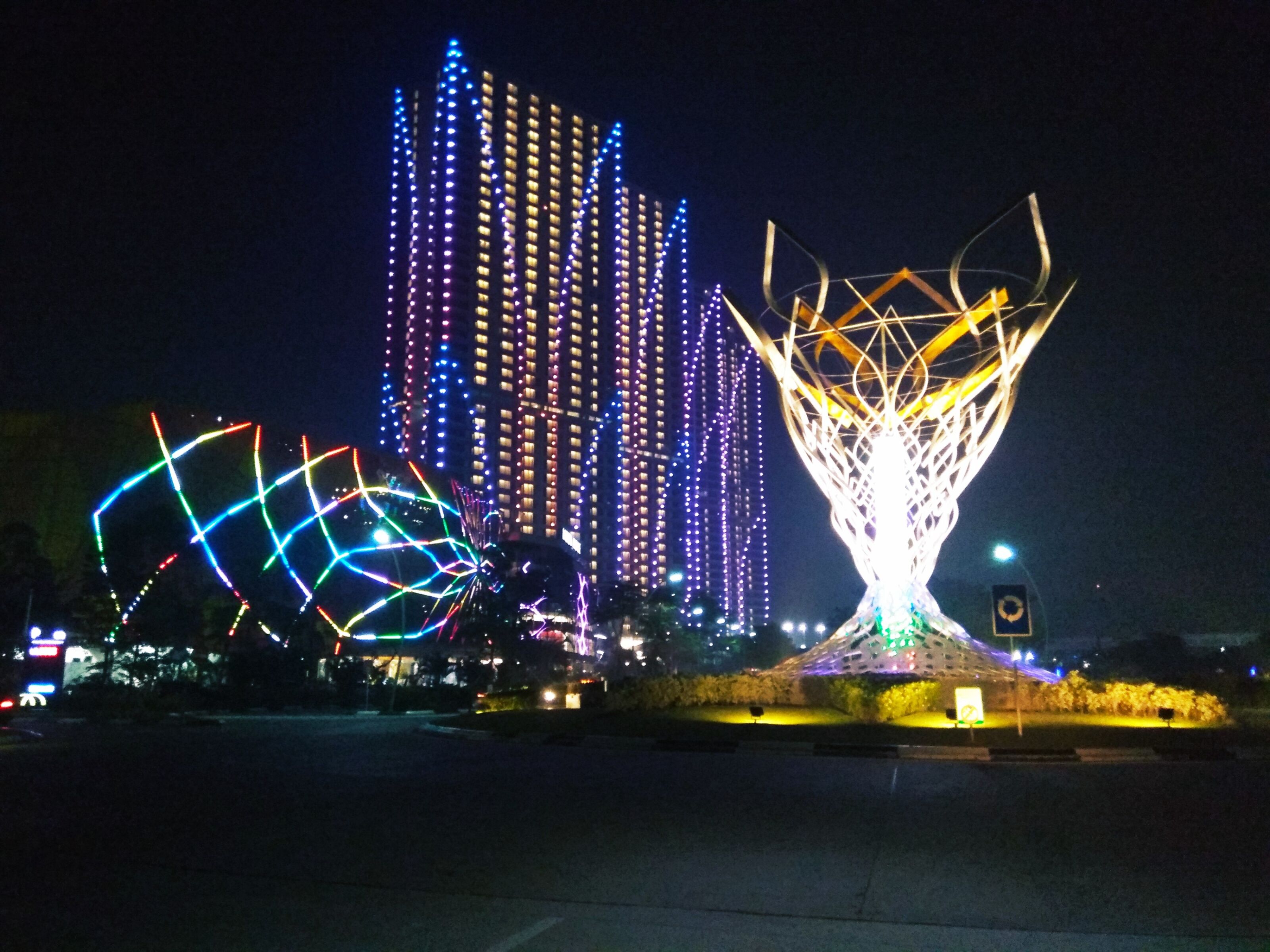 Nachtansicht einer Skyline mit beleuchteten Gebäuden und geometrischen Lichtinstallationen.
