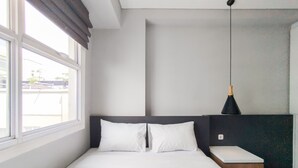 A modern hotel room with a large bed, a bedside table, a hanging light fixture, and a window with a view of buildings outside. - Stylish 1Br Apartment Parahyangan Residence (Bandung)