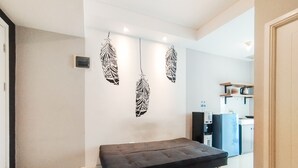 A modern living room with a sofa, decorative wall art, and a kitchen area in the background. - Stylish 1Br Apartment Parahyangan Residence (Bandung)