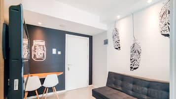A modern living room with a dark accent wall, a grey sofa, two white chairs, and decorative wall art.