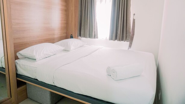 A double bed with white linens, a wooden headboard, and a window with curtains.