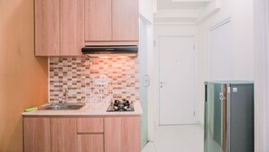 A compact kitchen with wooden cabinets, a tiled backsplash, a stainless steel sink, and a built-in gas stove.