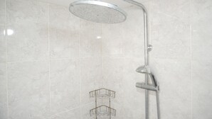 A shower with a rain showerhead and a handheld showerhead, a metal rack, and a tiled wall. - Good Deal And Homey Studio Bassura City Apartment (Jakarta)