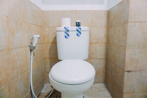 A bathroom with a white toilet, beige tiles, and a shower hose. - Best Deal And Restful 2Br Green Pramuka City Apartment (Jakarta)