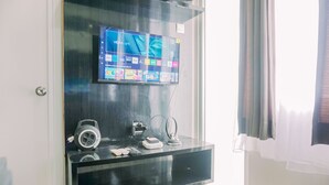 Ein modernes Wohnzimmer mit einem Flachbildfernseher, der an einer Glaswand angebracht ist, einer eleganten schwarzen Unterhaltungseinrichtung darunter und einem großen Fenster mit transparenten Vorhängen.