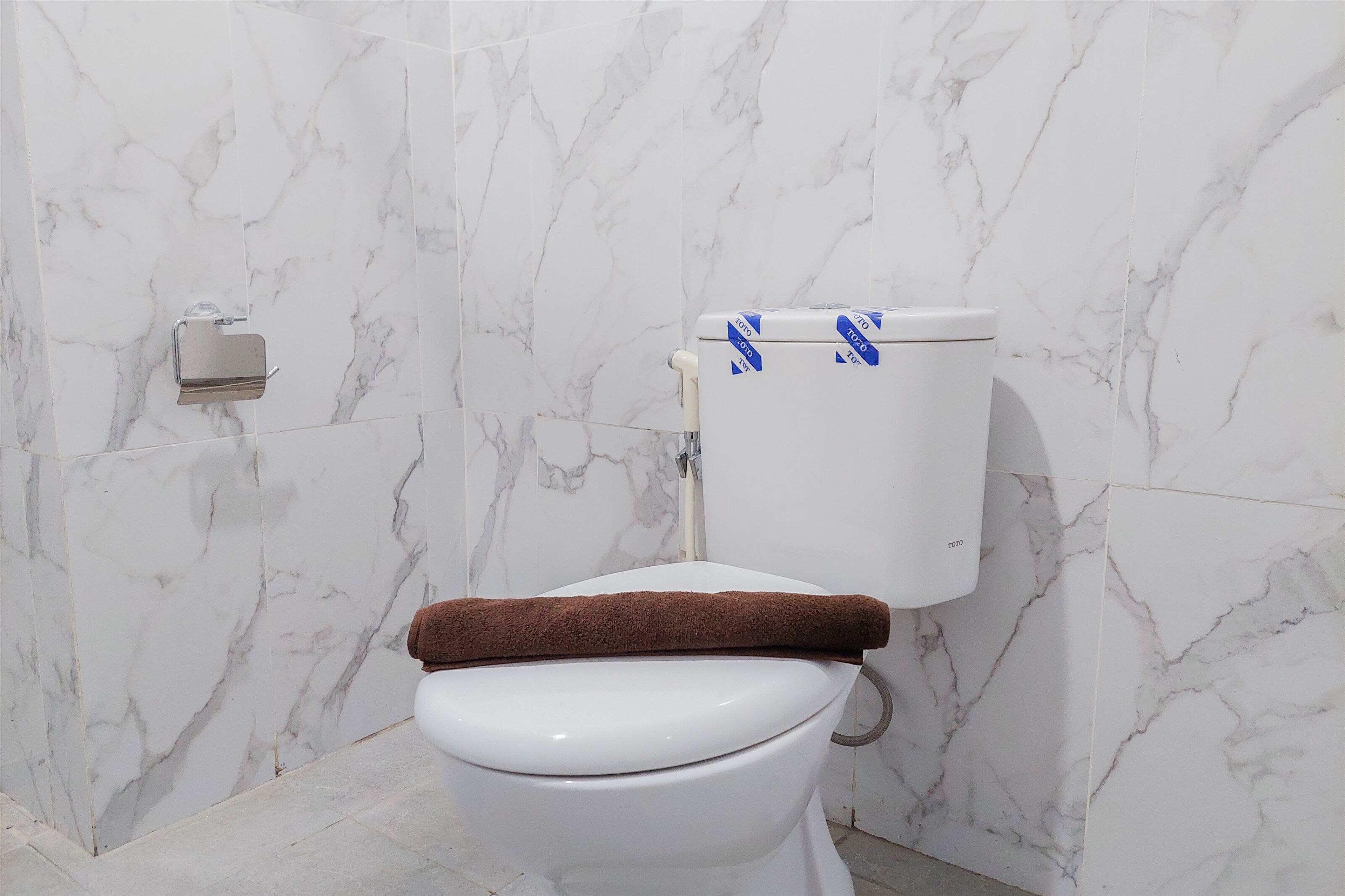 A bathroom with a white toilet, marble walls, and a towel placed on the seat.
