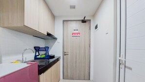 A narrow kitchen with wooden cabinets, a sink, and a door with a fire safety sign. - Good Deal And Homey Studio Apartment Anwa Residence Bintaro (South Tangerang)