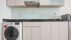 A compact kitchen with a built-in washing machine, a stainless steel sink, and light wood cabinetry.