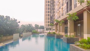 A swimming pool area with a high-rise building in the background. - Good Choice And Restful Studio At Transpark Cibubur Apartment Near Mall (Depok)