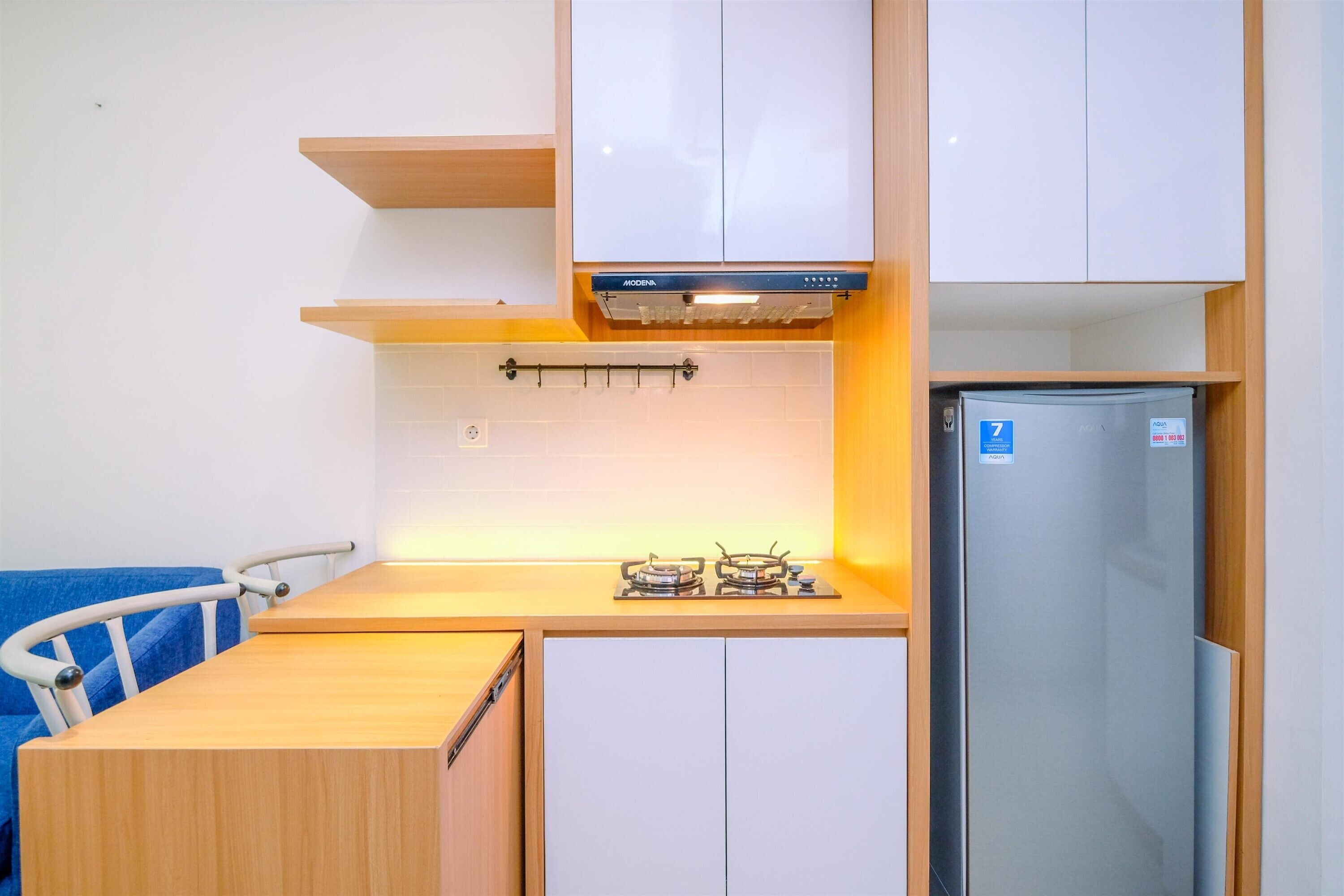 Une cuisine compacte dotée d’une cuisinière à gaz intégrée, d’un réfrigérateur et de meubles de cuisine blancs.