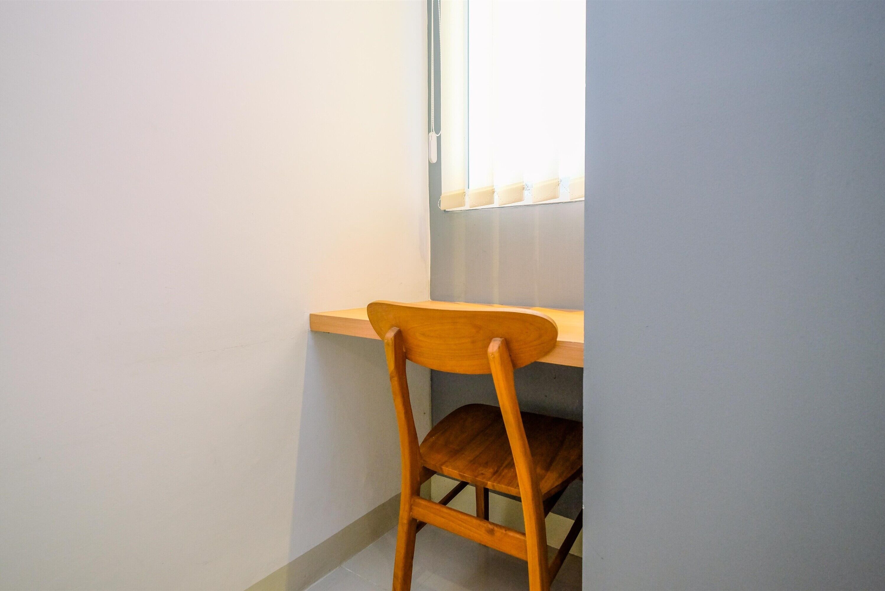 A corner room with a wooden chair, a window with blinds, and a white wall.