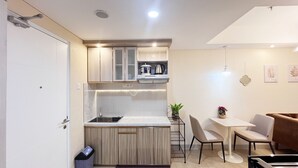 A compact kitchen with modern appliances, a dining area with a table and chairs, and a small potted plant. - Good Deal And Homey 1Br Tamansari Skylounge Makassar Apartment (Makassar)