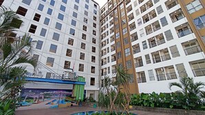 A multi-story residential building with balconies, a swimming pool, and a mural advertising a nearby attraction. - Good Deal And Homey 1Br Tamansari Skylounge Makassar Apartment (Makassar)