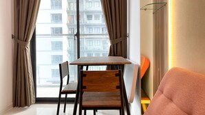 A modern living room with a dining table and chairs, a sofa, and a view of a high-rise building through large windows with curtains. - Good And Modern 2Br Daan Mogot City Apartment (Jakarta)