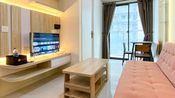 A modern living room with a flat-screen TV, wooden furniture, a pink sofa, and a view of the outside balcony. - Good And Modern 2Br Daan Mogot City Apartment (Jakarta)