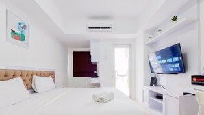 A hotel room with a bed, a TV, and a desk with a computer. - Cozy And Well Furnished Studio Baileys Apartment (South Tangerang)