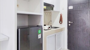 A compact kitchen with a refrigerator, a sink, and a wooden door. - Cozy And Well Furnished Studio Baileys Apartment (South Tangerang)