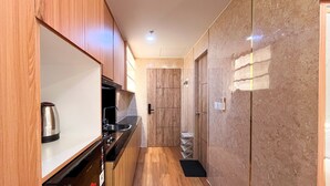 A narrow kitchen with wooden cabinets, a stainless steel kettle, and a marble backsplash.