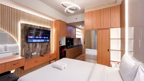 A hotel room with a bed, a TV mounted on a marble wall, wooden cabinets, a kitchen area, and a sliding door closet.
