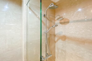 A shower with a handheld showerhead and a wall-mounted rainhead in a bathroom with marble walls.