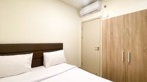 A hotel room with a bed, white linens, a wooden wardrobe, and an air conditioning unit. - Best Spacious And Homey 2Br At Meikarta Apartment (Cikarang)